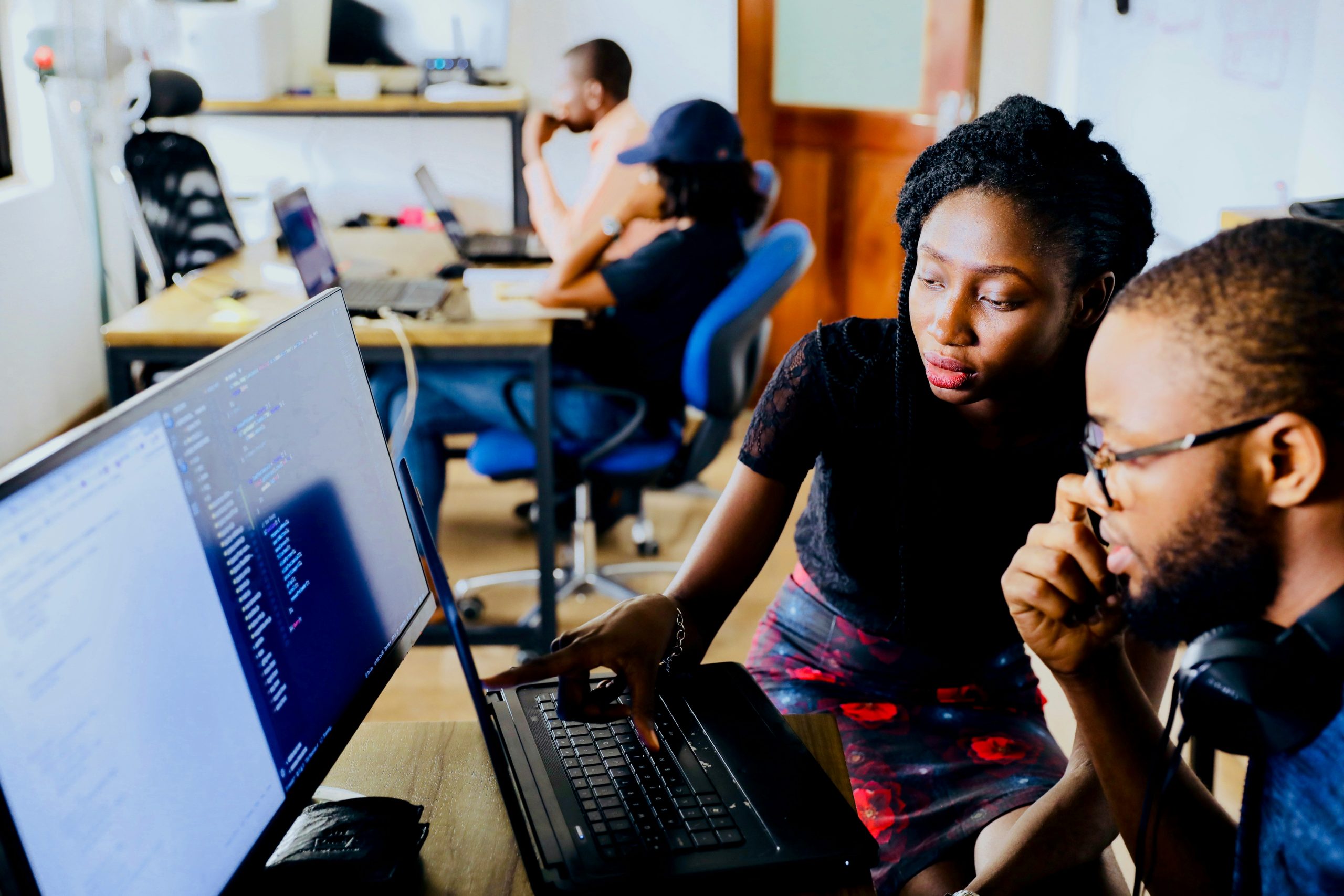 A man and a woman, both of African decent, working together on a computer. On the screen you see a design program that they are co-working together on. 