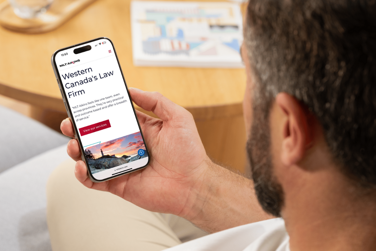 a man holding a phon with the browser open to the MLT Aikins website