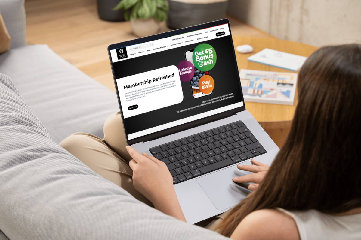 White woman on crew couch, laptop open on her lap, screen is showing the awards part of the Calgary co-op page